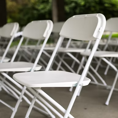 White ceremony chairs lined up for an outdoor wedding ceremony.