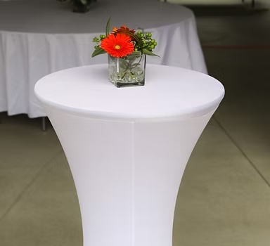 Cocktail table dressed in white spandex with a small floral arrangement.